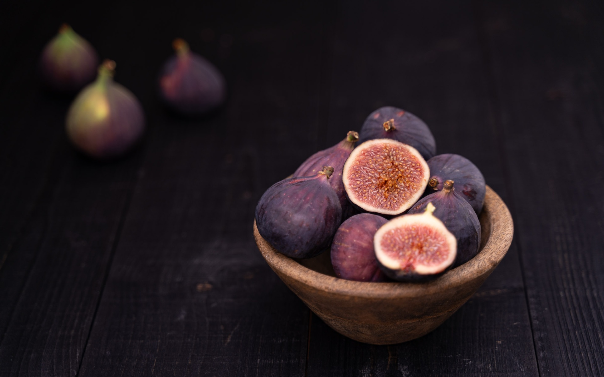 Fresh figs arranged in a wooden bowl against a dark studio backdrop
